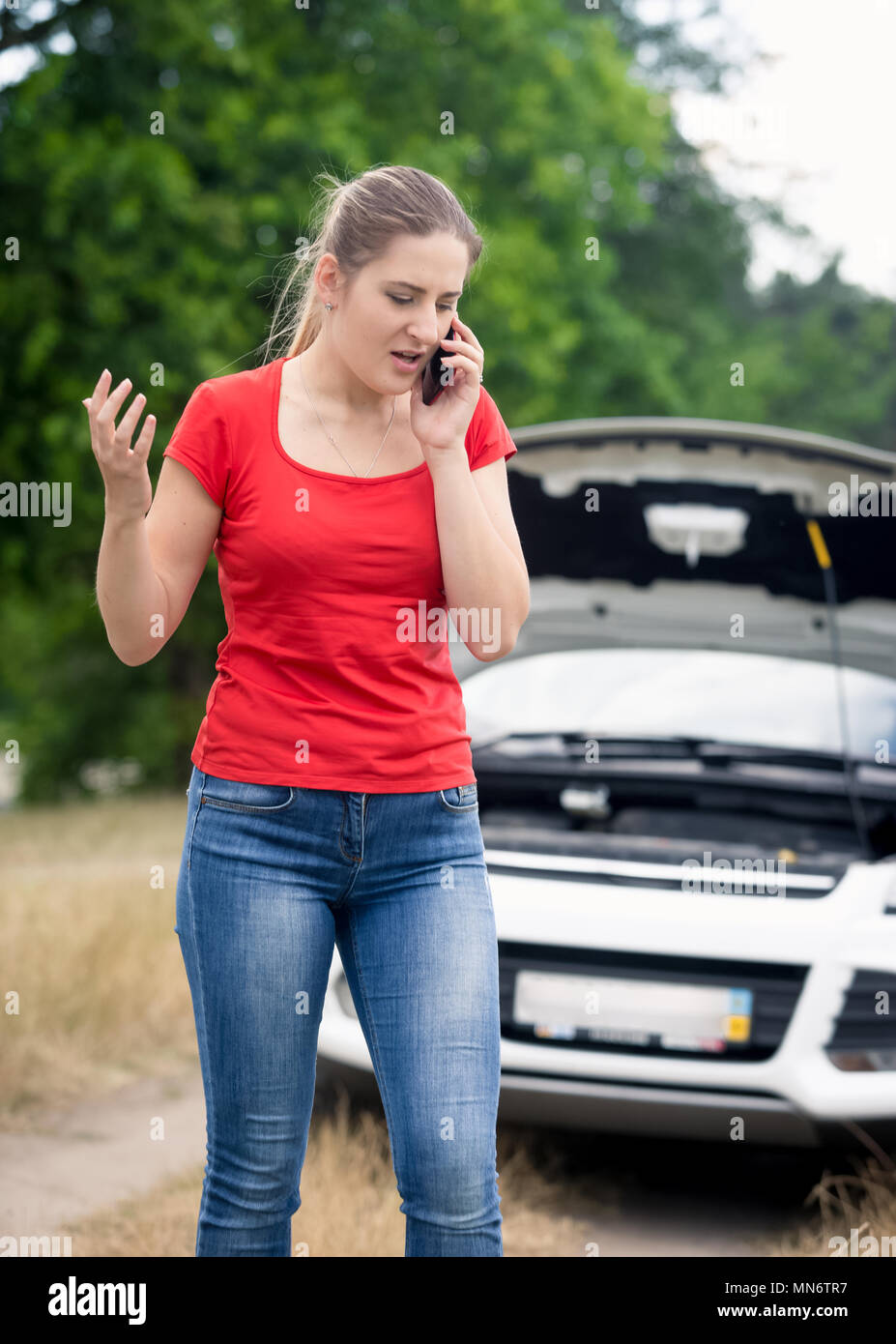 Portrait de jeune femme en colère de parler par téléphone et d'appeler l'assistance à sa voiture cassée dans le champ Banque D'Images