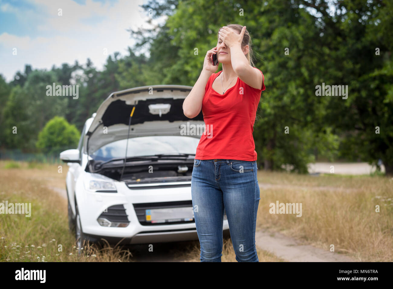 Jeune femme bouleversée debout à sa voiture cassée et l'appel d'assistance voiture Banque D'Images