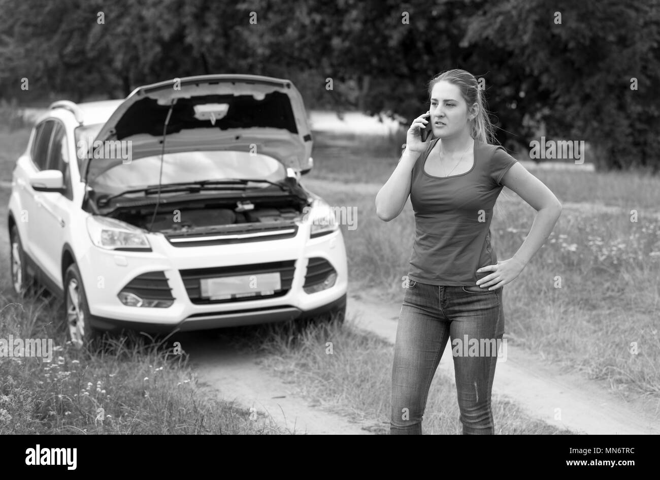 Image en noir et blanc de la jeune femme en colère parlant à cause de son service de location de voiture cassée Banque D'Images