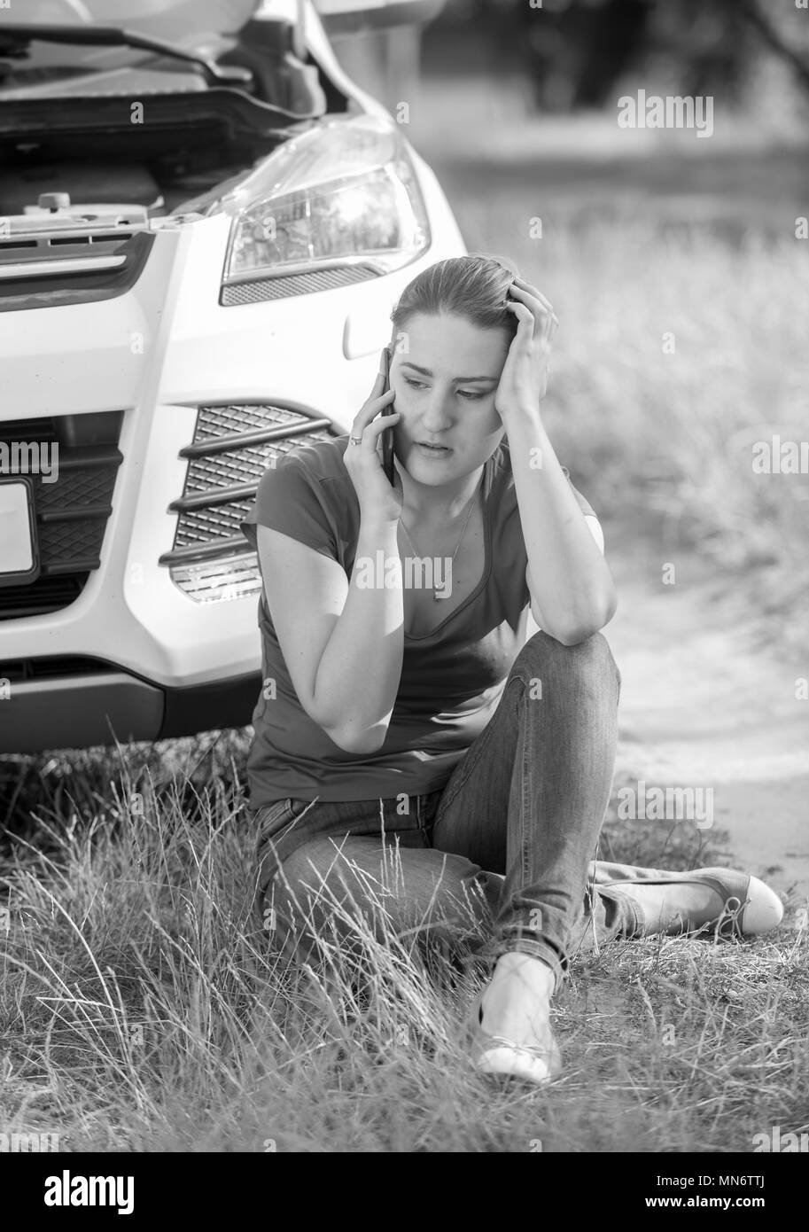 Image en noir et blanc de colère pleurer femme appelant un service en raison de son champ en automobile cassée Banque D'Images