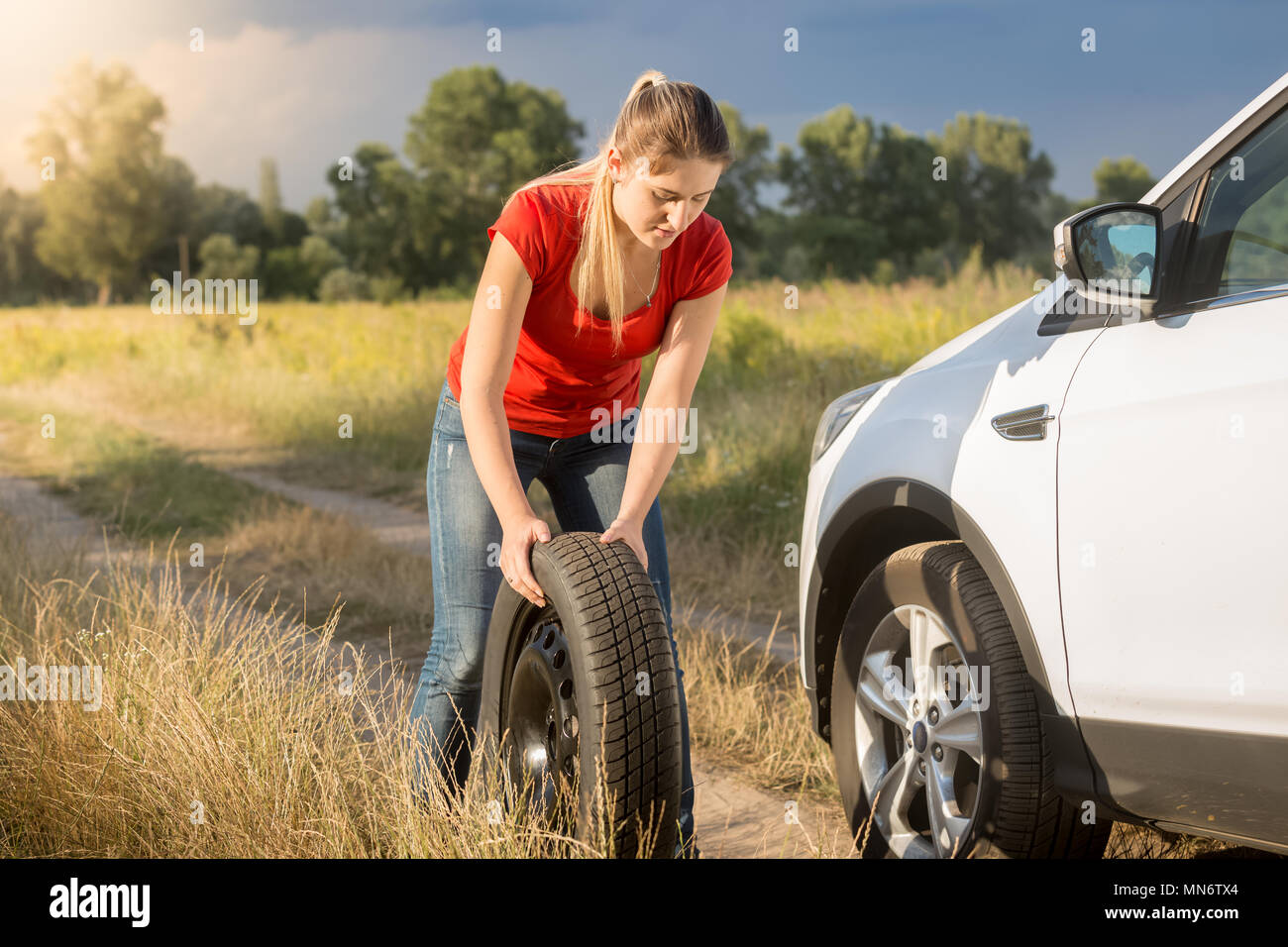 Jeune femme pour changer de roue de roulement des pneus flate sur sa voiture Banque D'Images