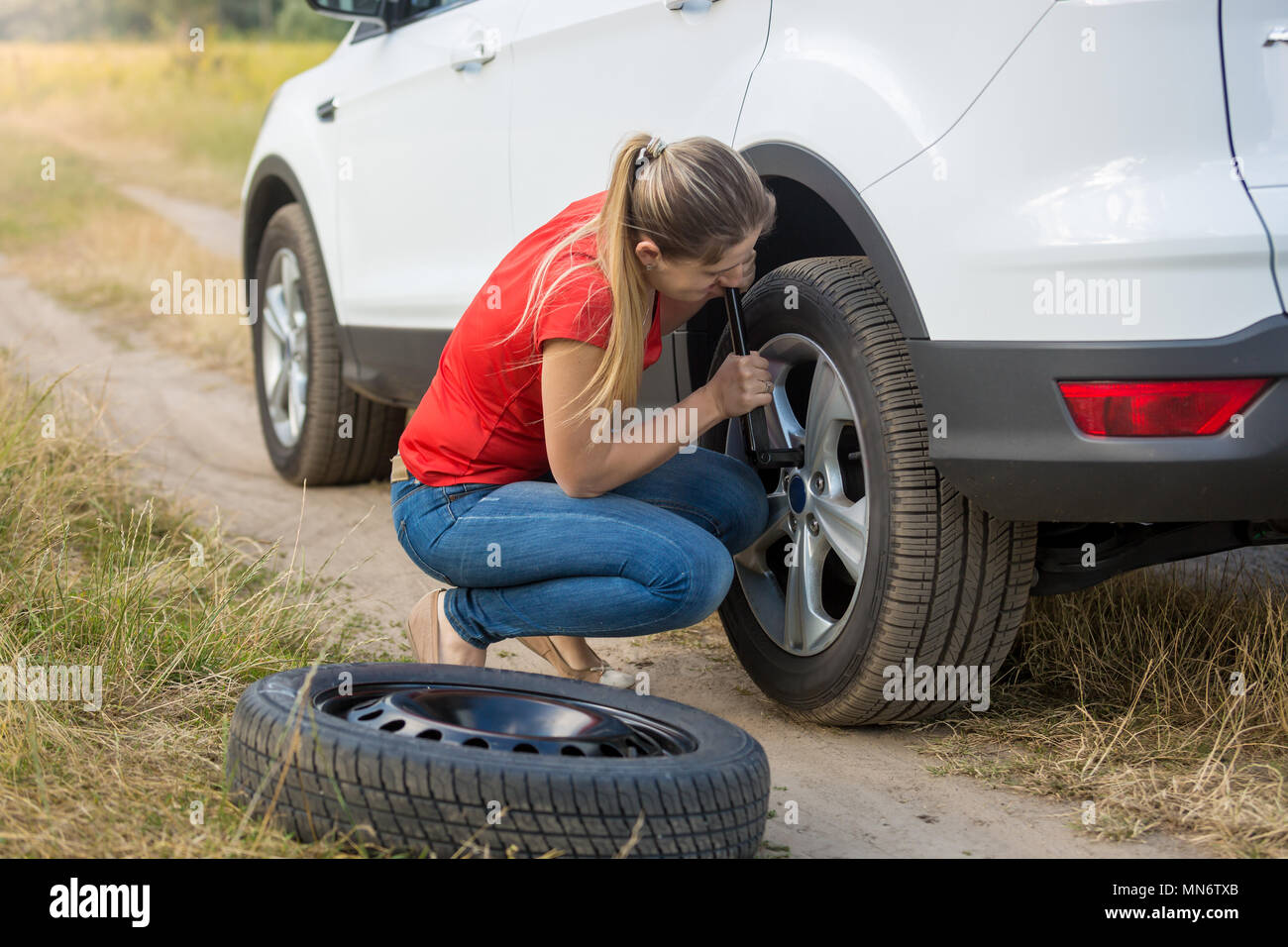 Jeune femme de dévisser les écrous de roue de voiture pour changer pneu plat Banque D'Images