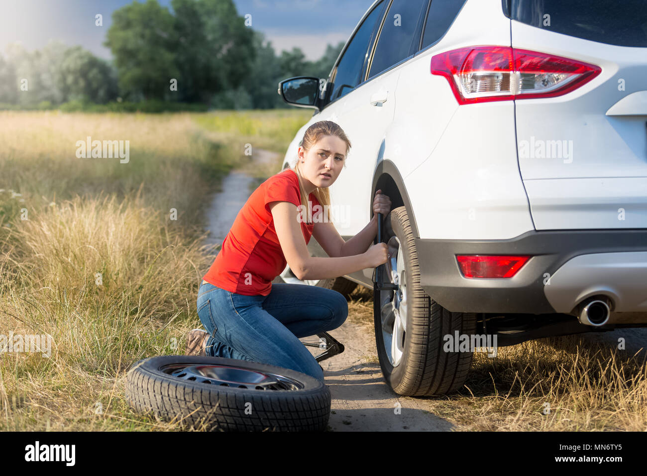 Jeune femme essayant de changer de pneu à plat et de dévisser les écrous de roue de voiture Banque D'Images