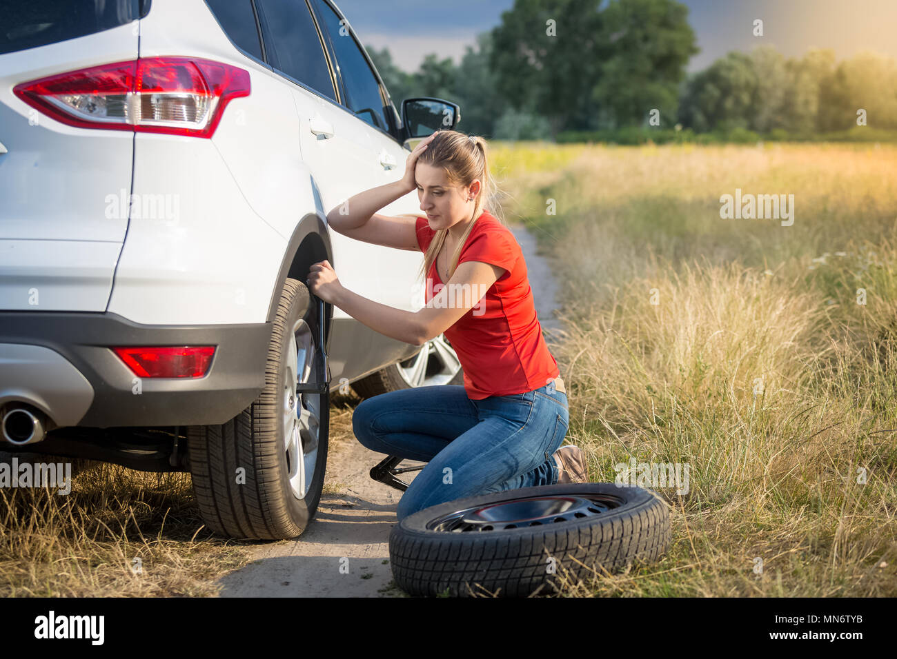 Jeune femme en colère à la recherche sur le pneu de sa voiture sur la route de campagne Banque D'Images