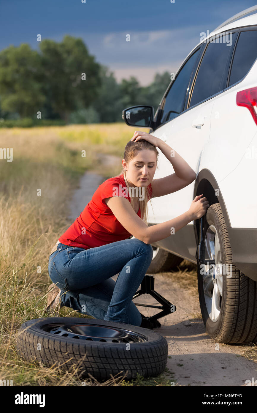 Jeune femme assise sur sa voiture avec pneu plat essayer de dévisser les écrous de roue Banque D'Images