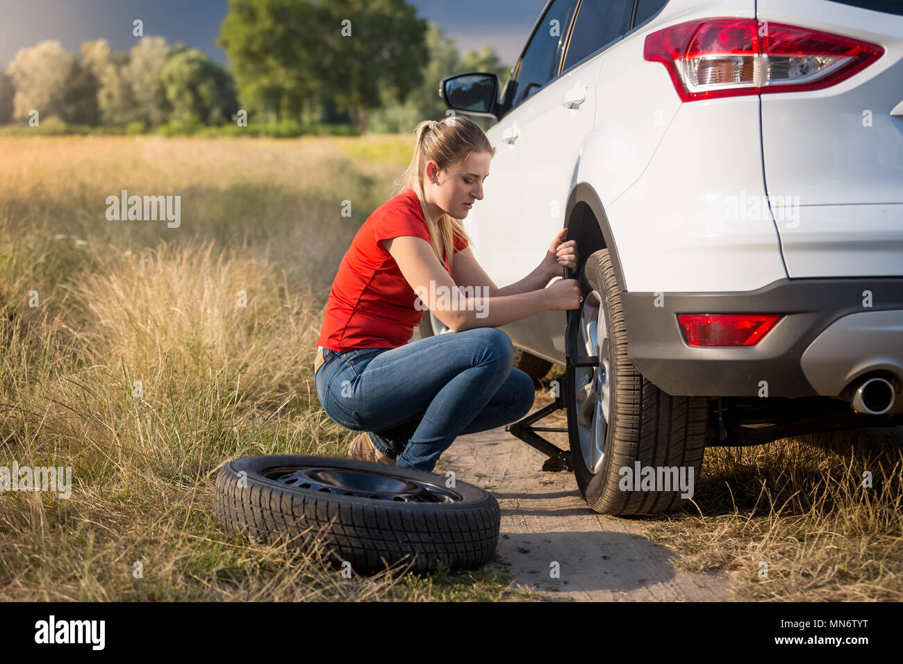 Jeune femme changer de roue de voiture sur la route déserte sur le terrain Banque D'Images