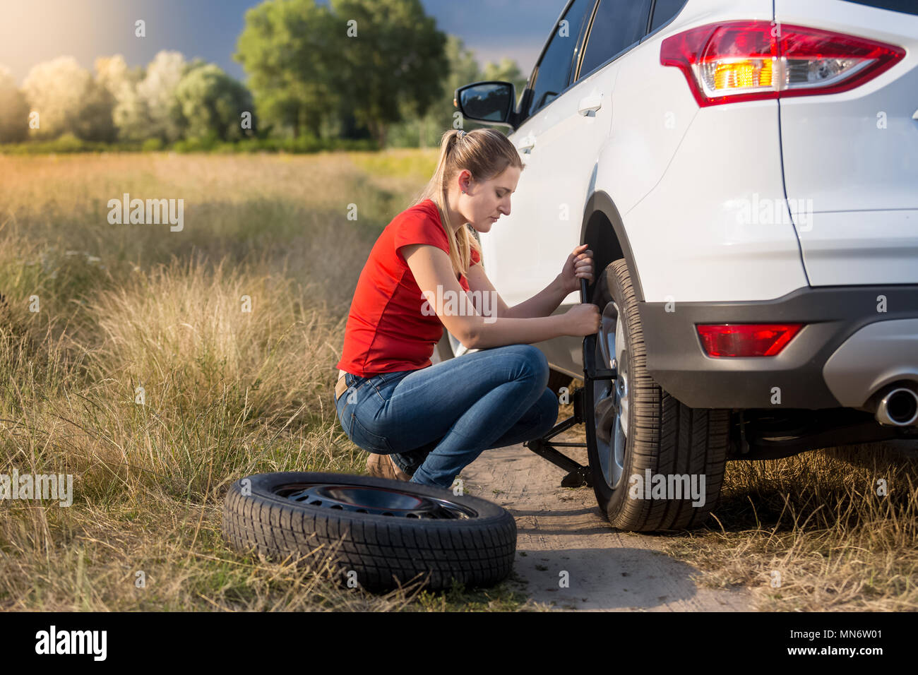 Jeune femme à l'aide d'un cric pour soulever sa voiture avec pneu plat et dévisser les écrous de roue Banque D'Images