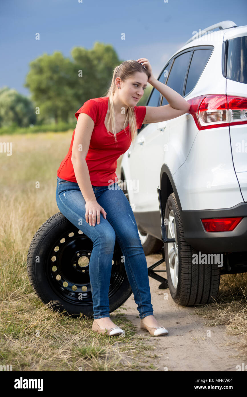 Colère jeune femme assise sur roue de secours de voiture cassée dans le champ Banque D'Images