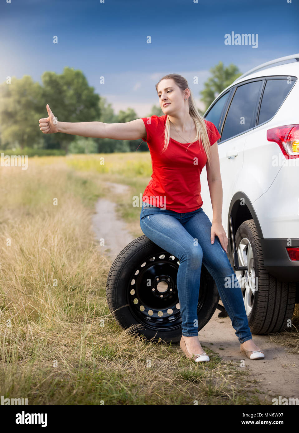 Jeune femme assise à son voiture cassée dans le champ et de l'autostop Banque D'Images