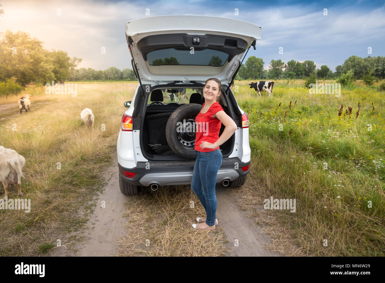 Jeune femme en tenant hors de la roue de secours coffre de voiture sur route de campagne Banque D'Images
