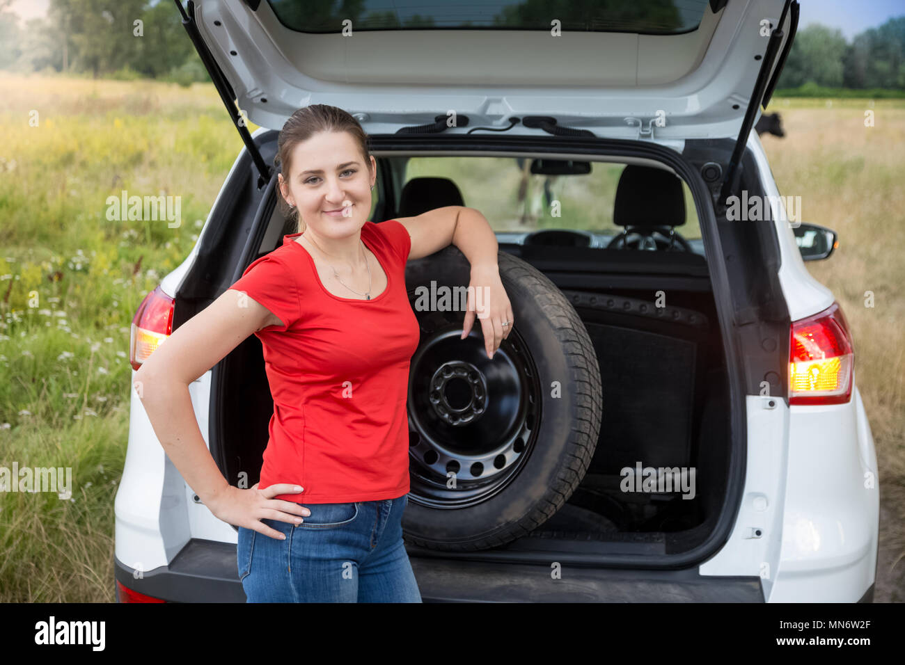 Portrait de jeune femme en tenant la roue de secours de voiture hors de ligne ouverte Banque D'Images