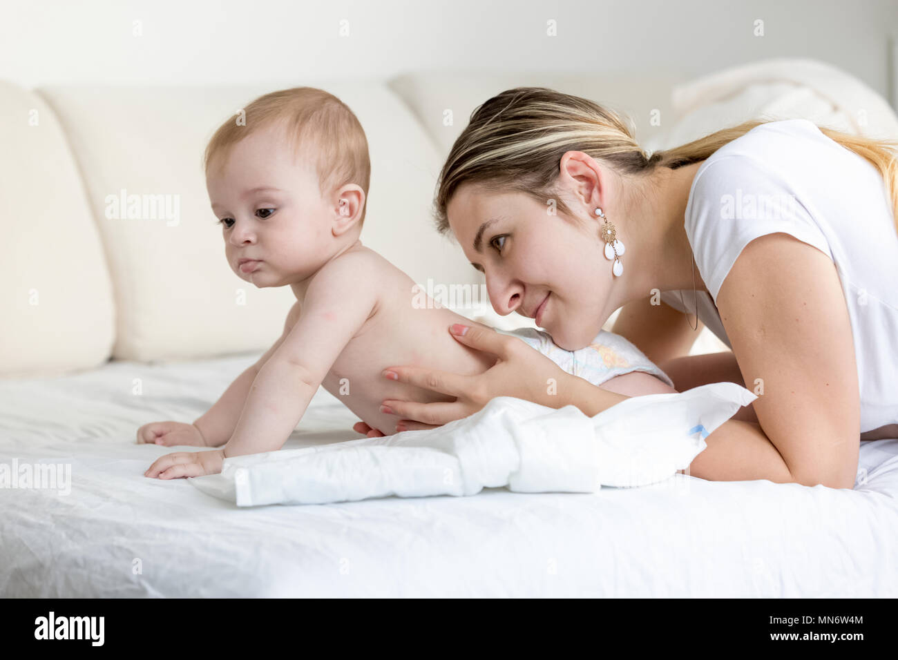 Portrait de belle jeune femme caressant et en regardant son bébé lying on bed Banque D'Images
