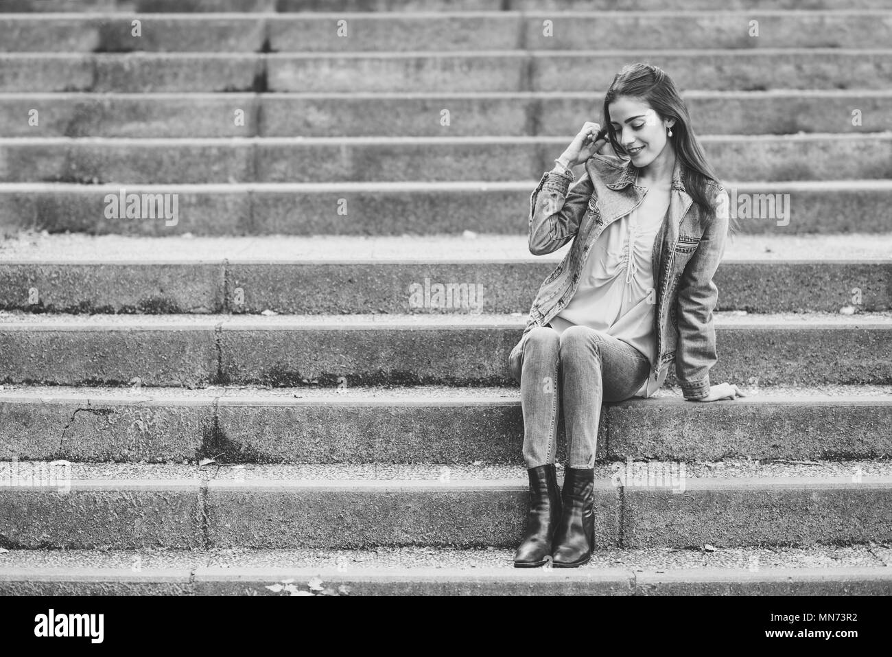 Jeune femme avec des cheveux de nice portant des vêtements décontractés en contexte urbain. Happy girl with wavy hairstyle assis en milieu urbain des escaliers. Banque D'Images