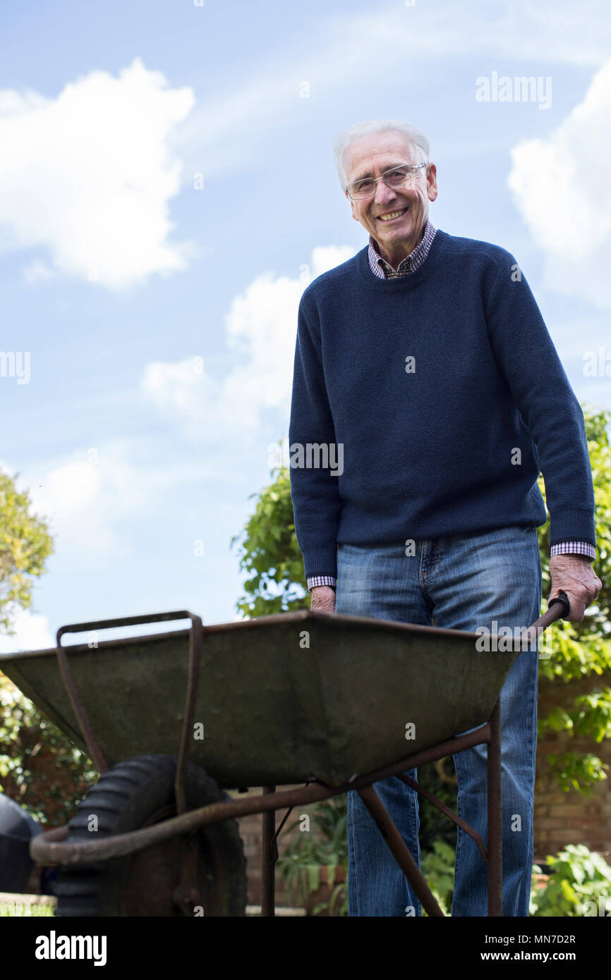 Portrait of Senior Man Pushing Barrow alors que le jardinage Banque D'Images