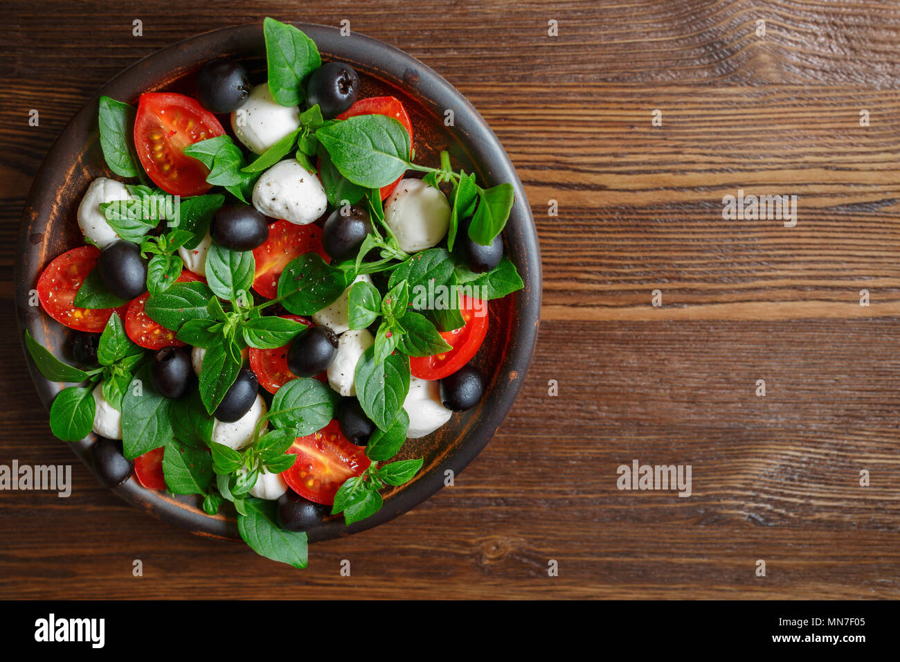 Salade italienne classique avec de la mozzarella, tomates, basilic, olives et huile d'olive. Caprese dans une cuvette d'argile sur un fond de bois. Vue de dessus, copiez l'espace. Banque D'Images