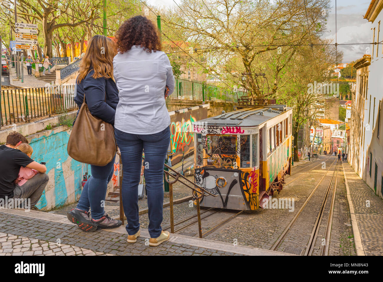 Scène de la rue de Lisbonne, vue arrière de deux jeunes femmes regardant un tram monter l'Elevador do Gloria dans le quartier Baixa du centre de Lisbonne, Portugal. Banque D'Images