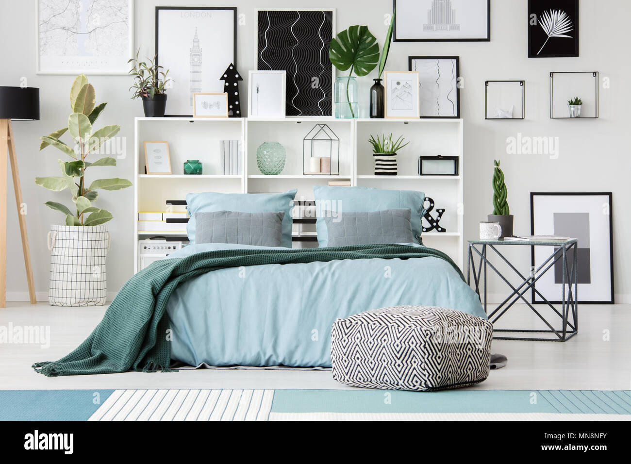 Pouf à motifs en face de lit bleu avec couverture verte dans la chambre  intérieur avec ficus et affiches Photo Stock - Alamy