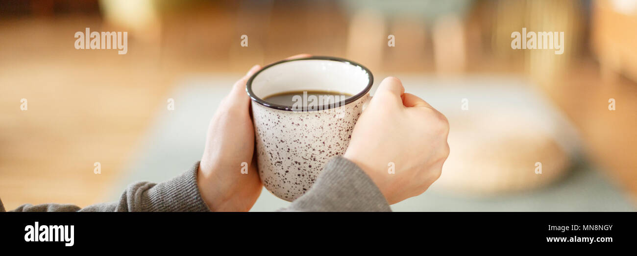 Photo en gros plan de woman's hands holding a white, metal mug avec plateau Banque D'Images