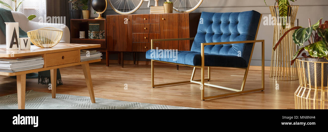 Fauteuil bleu royal avec gold frame standing in vintage salon intérieur avec armoire en bois et une table basse avec des magazines Banque D'Images