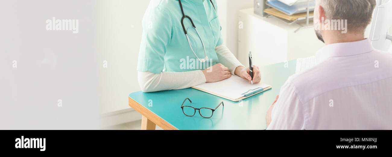 Médecin en vert frotte une entrevue et écrire les informations de l'historique médical du patient lors d'une consultation Banque D'Images