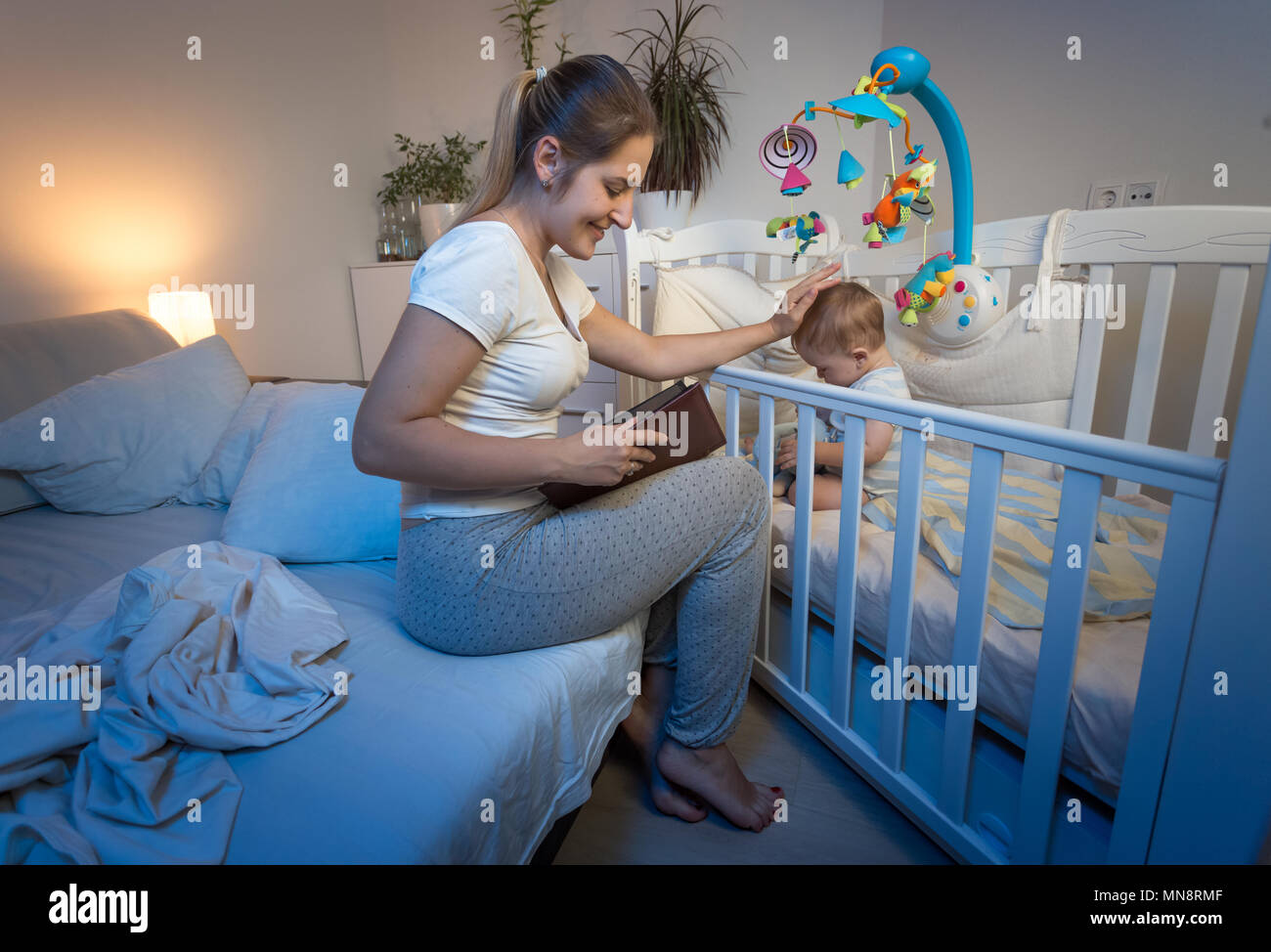 Portrait Of Young Smiling Mother En Pyjama Assis Sur Le Lit Et De La Lecture Livre A Son Bebe Avant D Aller Dormir Photo Stock Alamy