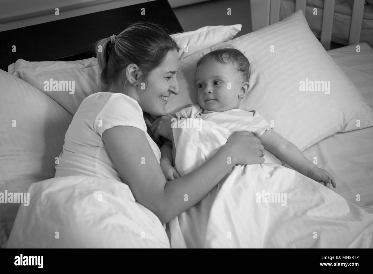 Portrait of smiling baby boy looking at heureux mère couchant avec lui au lit Banque D'Images