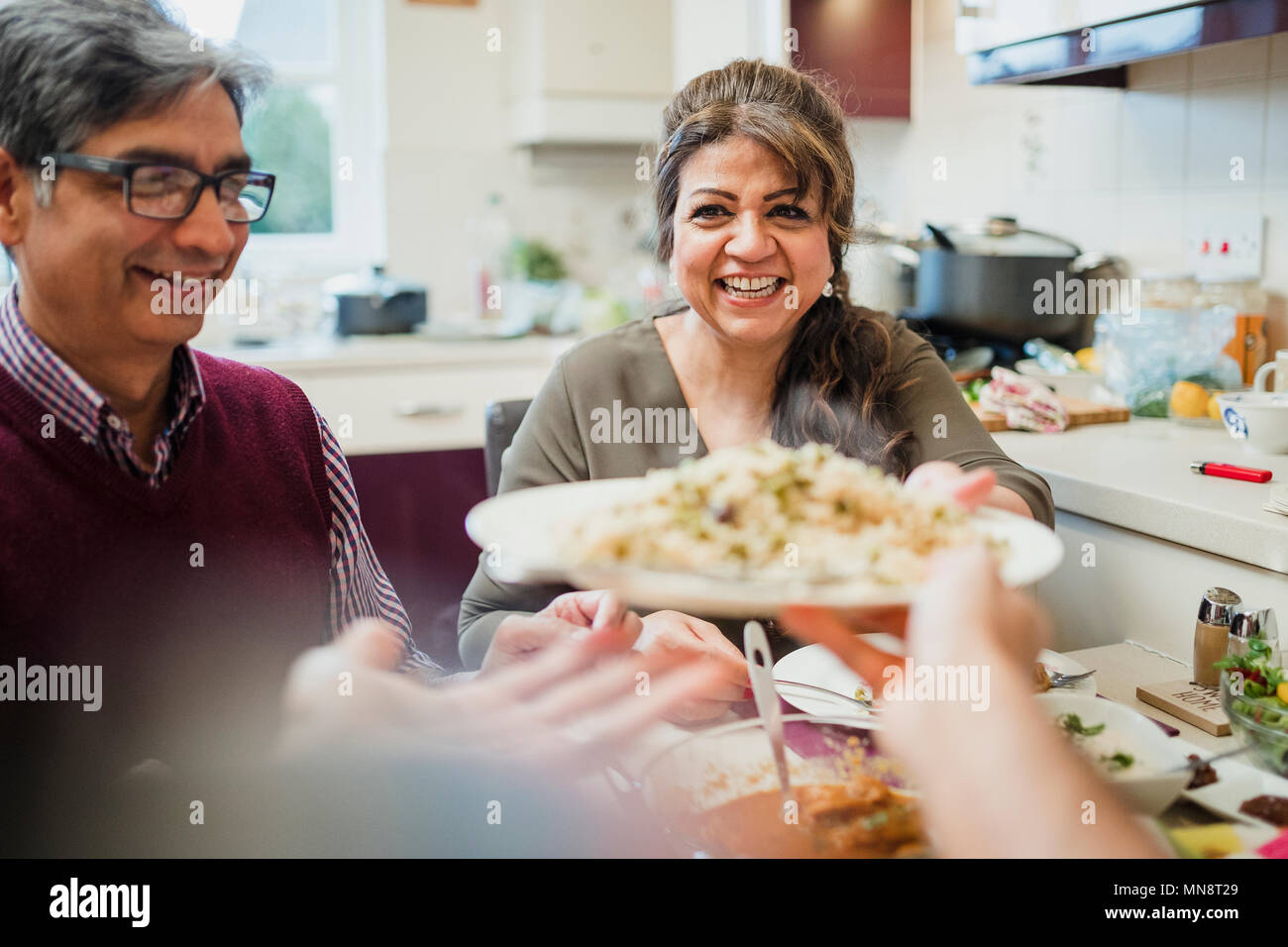 Point de vue tourné d'une mère mature passant une portion de curry et de riz pour son fils à la table à manger. Banque D'Images