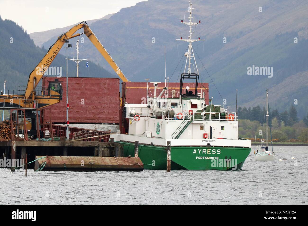 Un Ayress Portsmouth bateau amarré à la Sainte Loch, Firth of Clyde, en Écosse, au Royaume-Uni d'être chargé de grumes coupées par un Multidocker. Banque D'Images