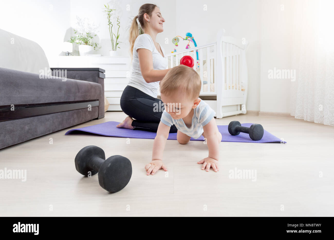 Adorable bébé garçon ramper sur le plancher tandis que sa mère à la maison de remise en forme pratique Banque D'Images