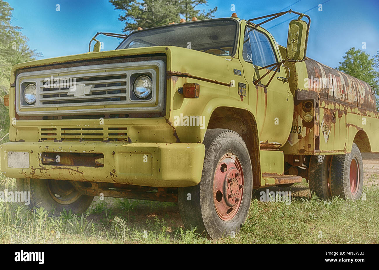 'Le jaune' un grand camion jaune rouille et abandonnés dans un champ d'herbe verte avec ciel bleu Banque D'Images