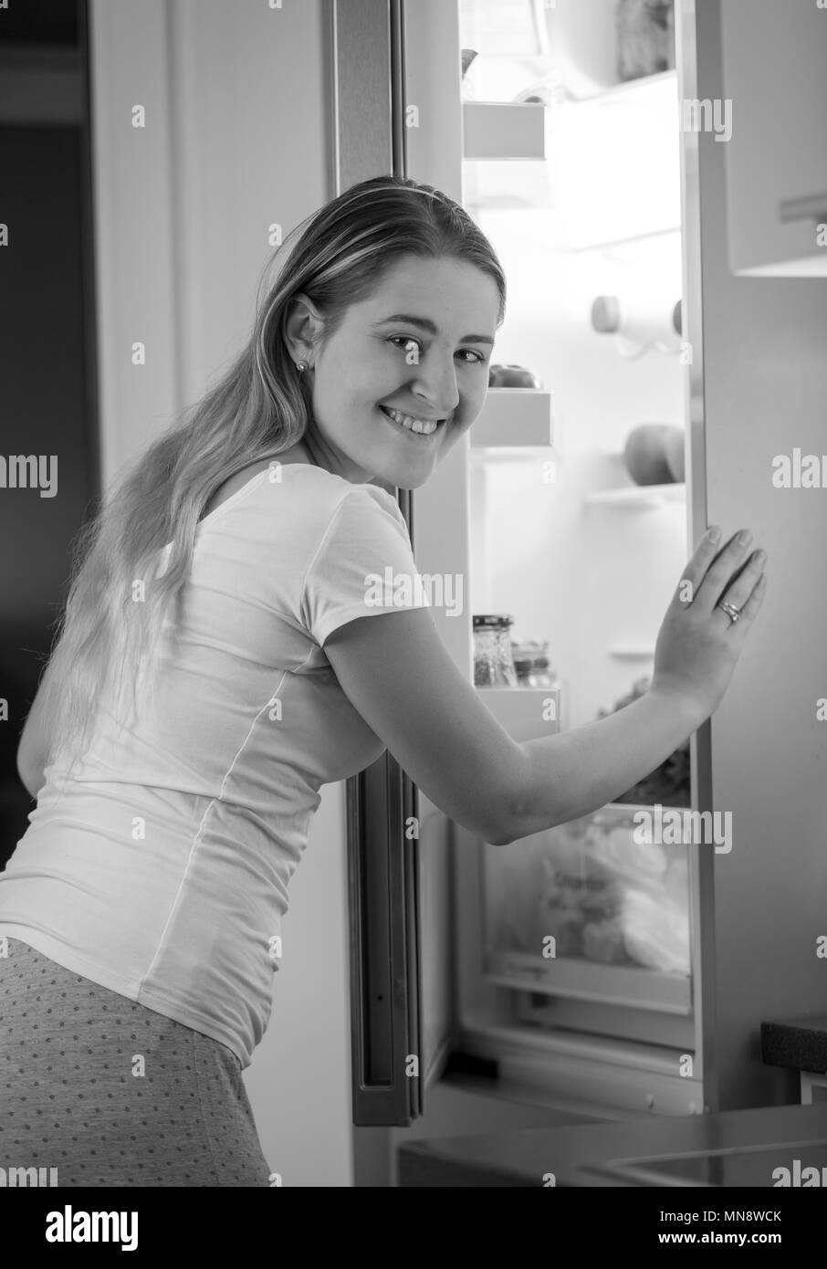 Image en noir et blanc de la jeune femme en pyjama debout à ouvrir réfrigérateur dans la nuit Banque D'Images