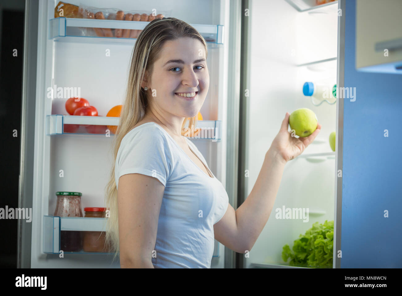 Portrait of smiling young woman with fresh green apple hors de nuit au réfrigérateur). Banque D'Images