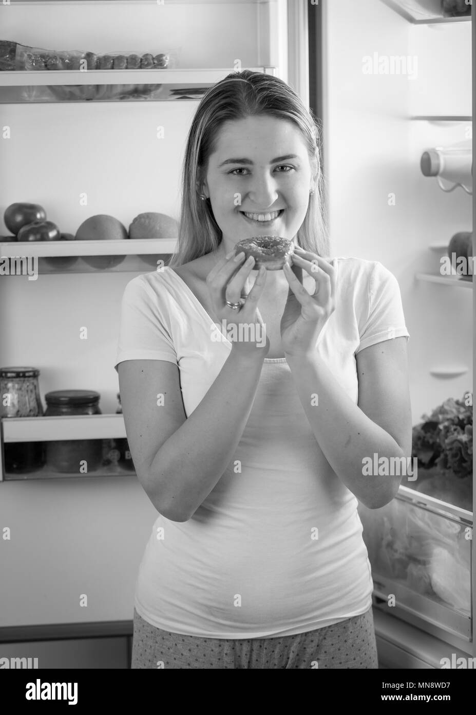 Portrait of smiling young woman posing with sweet donut sur cuisine de nuit Banque D'Images