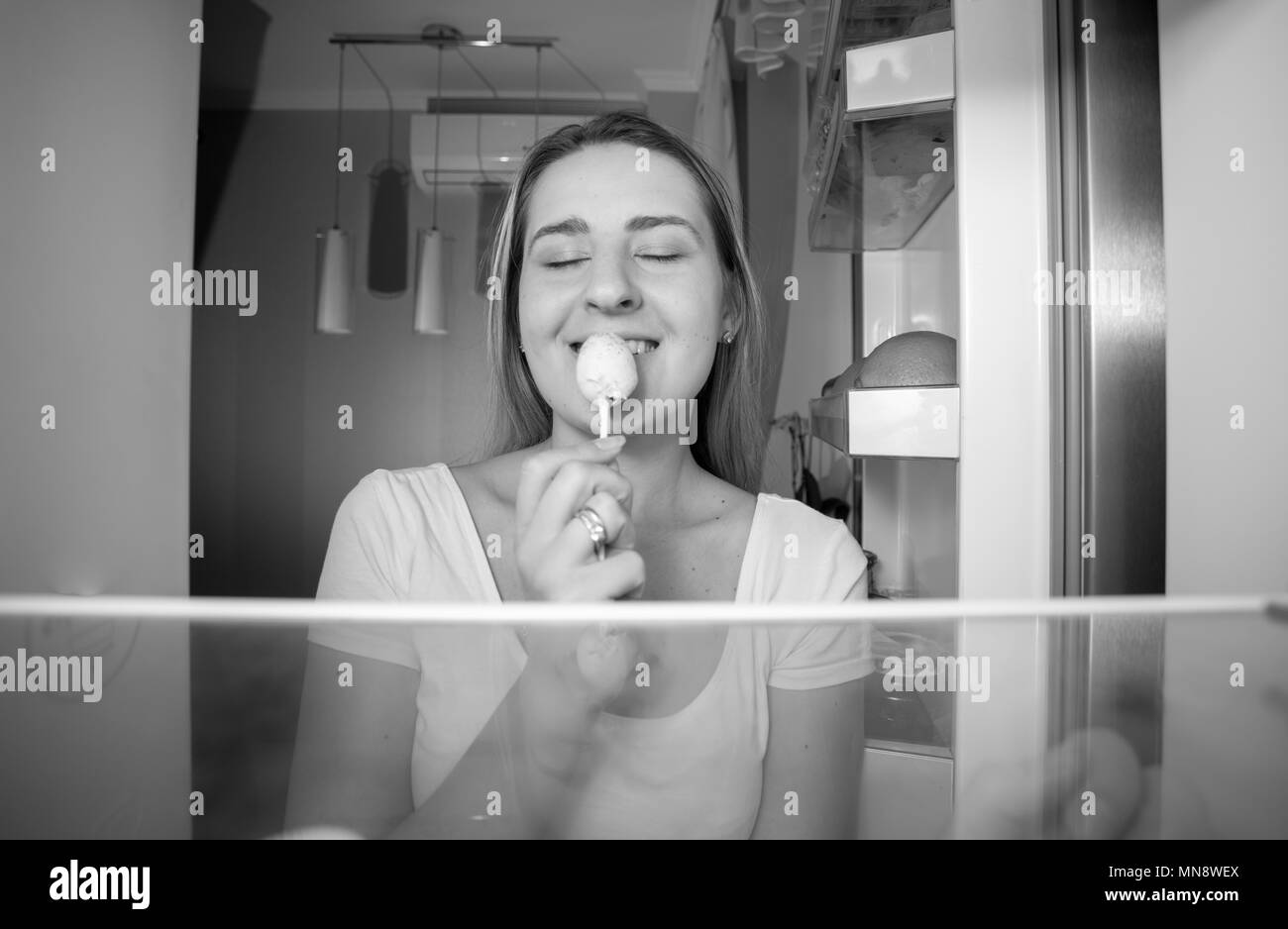 Portrait of smiling young woman standing au réfrigérateur et manger une sucette Banque D'Images