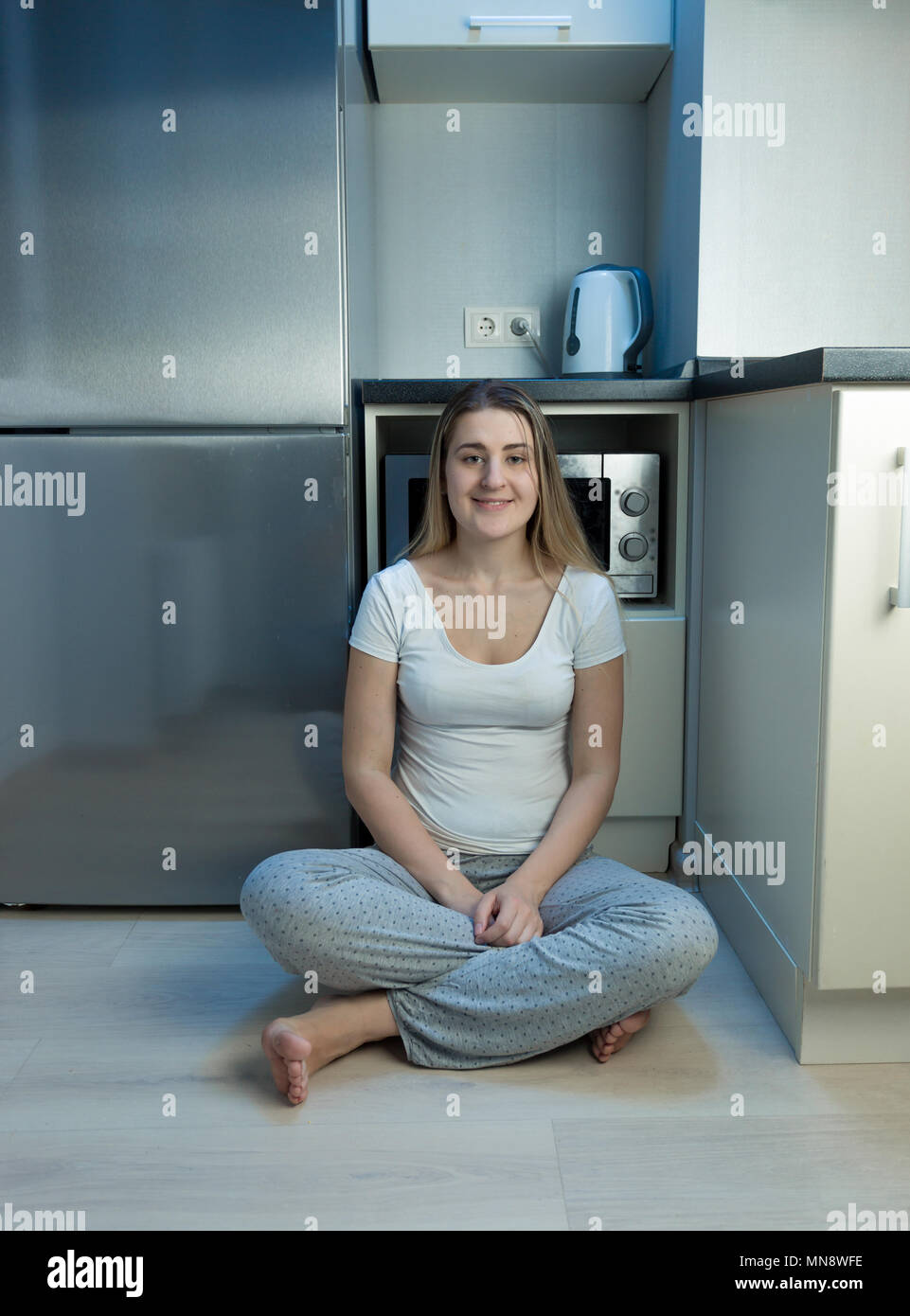 Jeune femme de la faim en pyjama assis sur marbre au réfrigérateur Banque D'Images