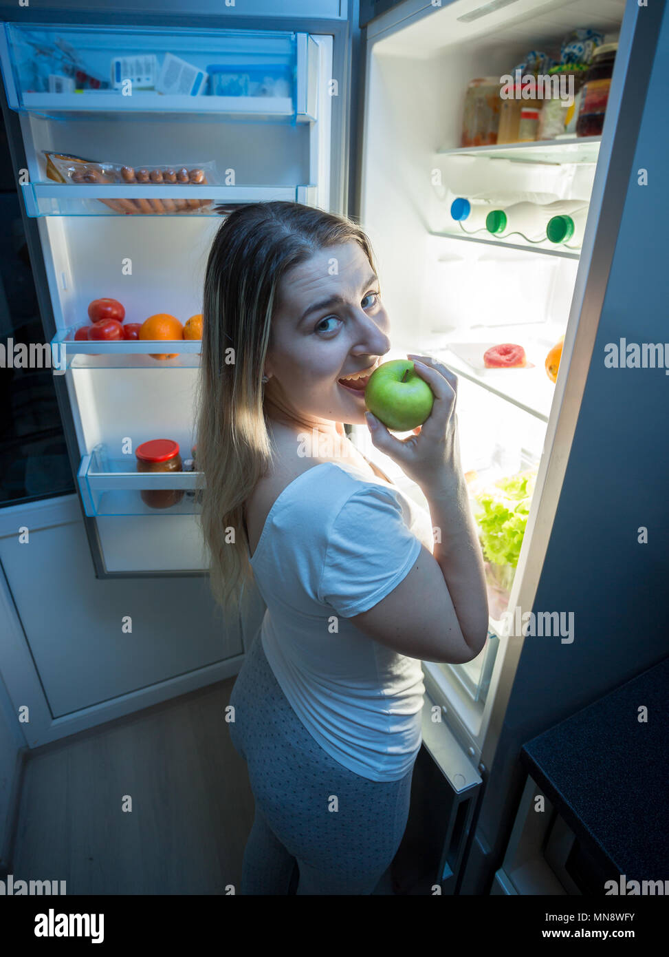 Portrait de jeunes affamés woman eating fresh green apple sur la cuisine de nuit Banque D'Images