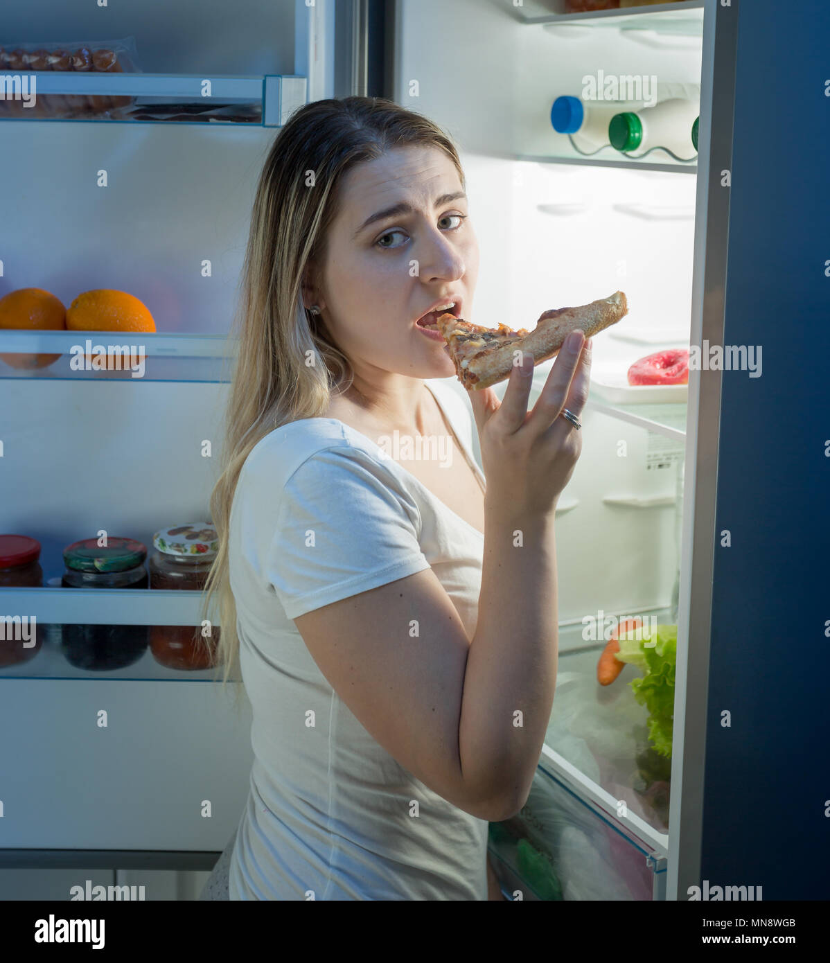 Jeune femme à la coupe faim nuit debout sur cuisine et manger des pizzas. Concept de la mauvaise alimentation et de la nutrition Banque D'Images