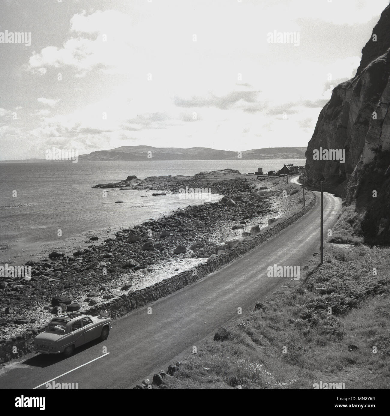 Années 1950, historiques, une voiture roulant le long d'une route calme, vide, la magnifique route côtière de la chaussée en Irlande du Nord. Cette belle et spectaculaire tronçon de route est toujours aussi belle qu'elle l'était alors et est considéré comme l'un des plus grands lecteurs que un automobiliste peut faire. Banque D'Images