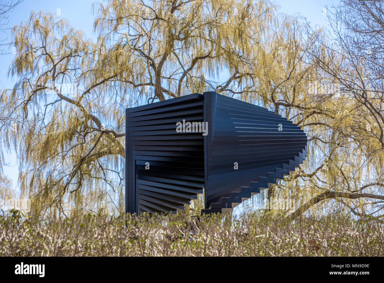 Grande sculpture extérieure noir avec un grand saule derrière elle Banque D'Images