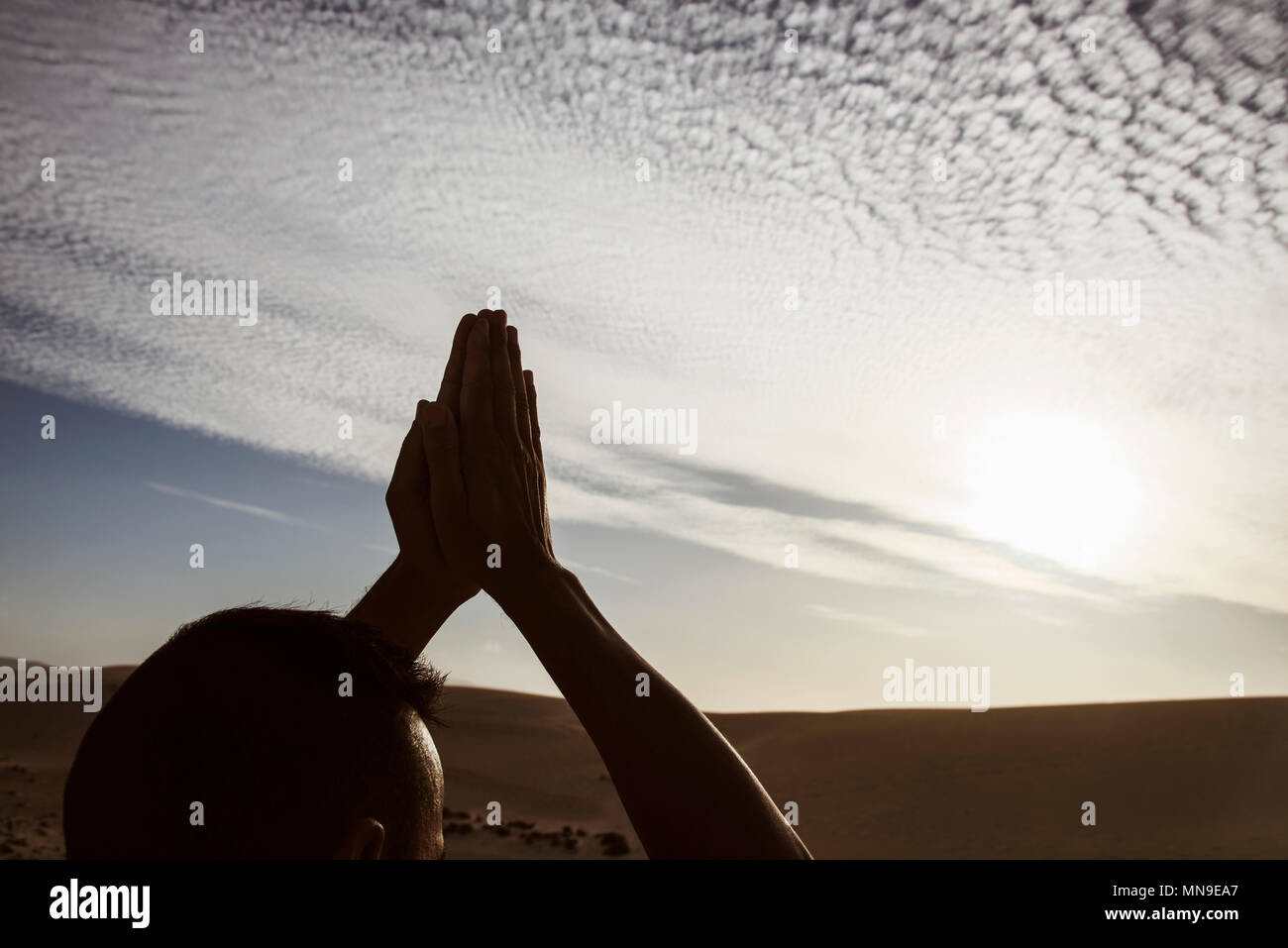Closeup of a young caucasian man practicing yoga à l'extérieur, contre un ciel nuageux, avec le soleil en arrière-plan Banque D'Images