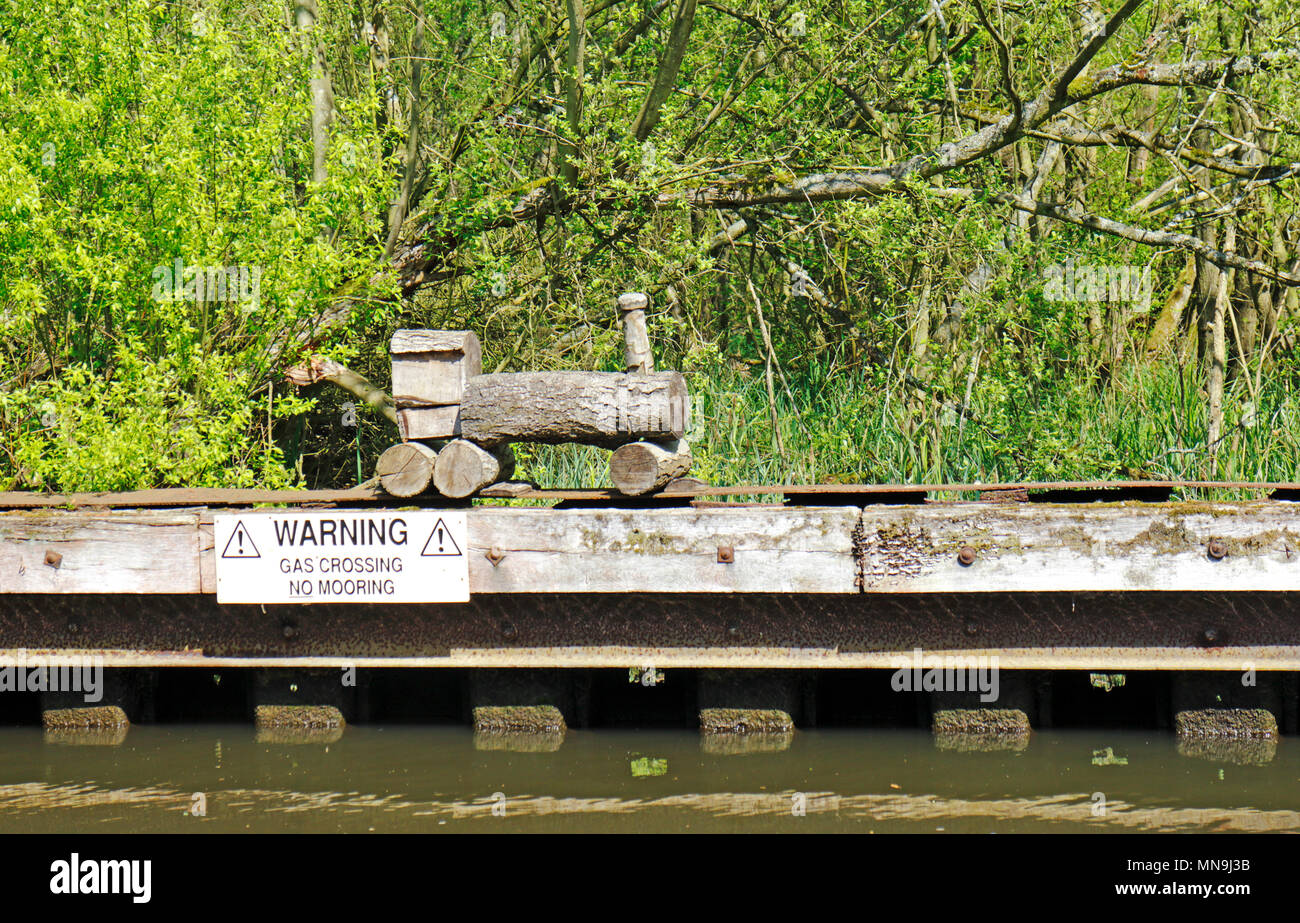 Un modèle naïf train en bois par un gazoduc traversant sur la rivière Bure près de Belaugh, Norfolk, Angleterre, Royaume-Uni, Europe. Banque D'Images