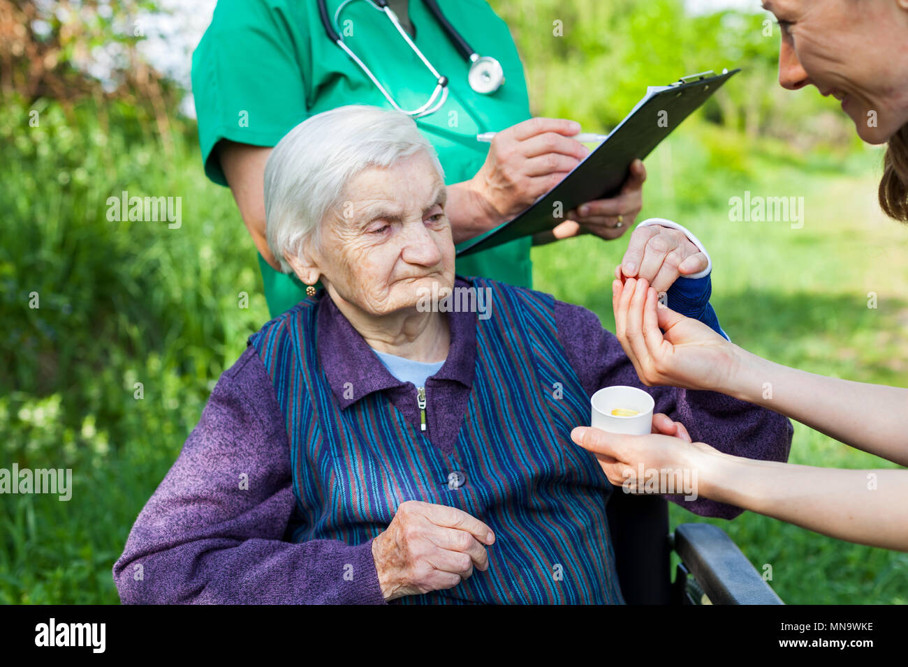 Personnes âgées femme malade recevant les pilules d'une infirmière, médecin écrit prescription médicale dans l'arrière-plan Banque D'Images