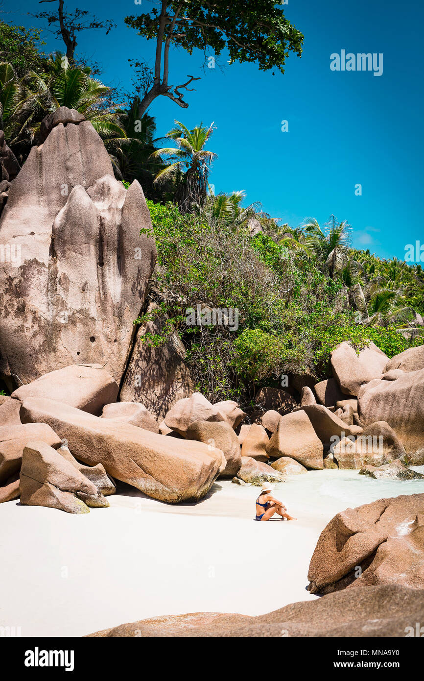 Side view of mid adult woman in bikini sitting at beach contre ciel bleu clair, les Seychelles Banque D'Images