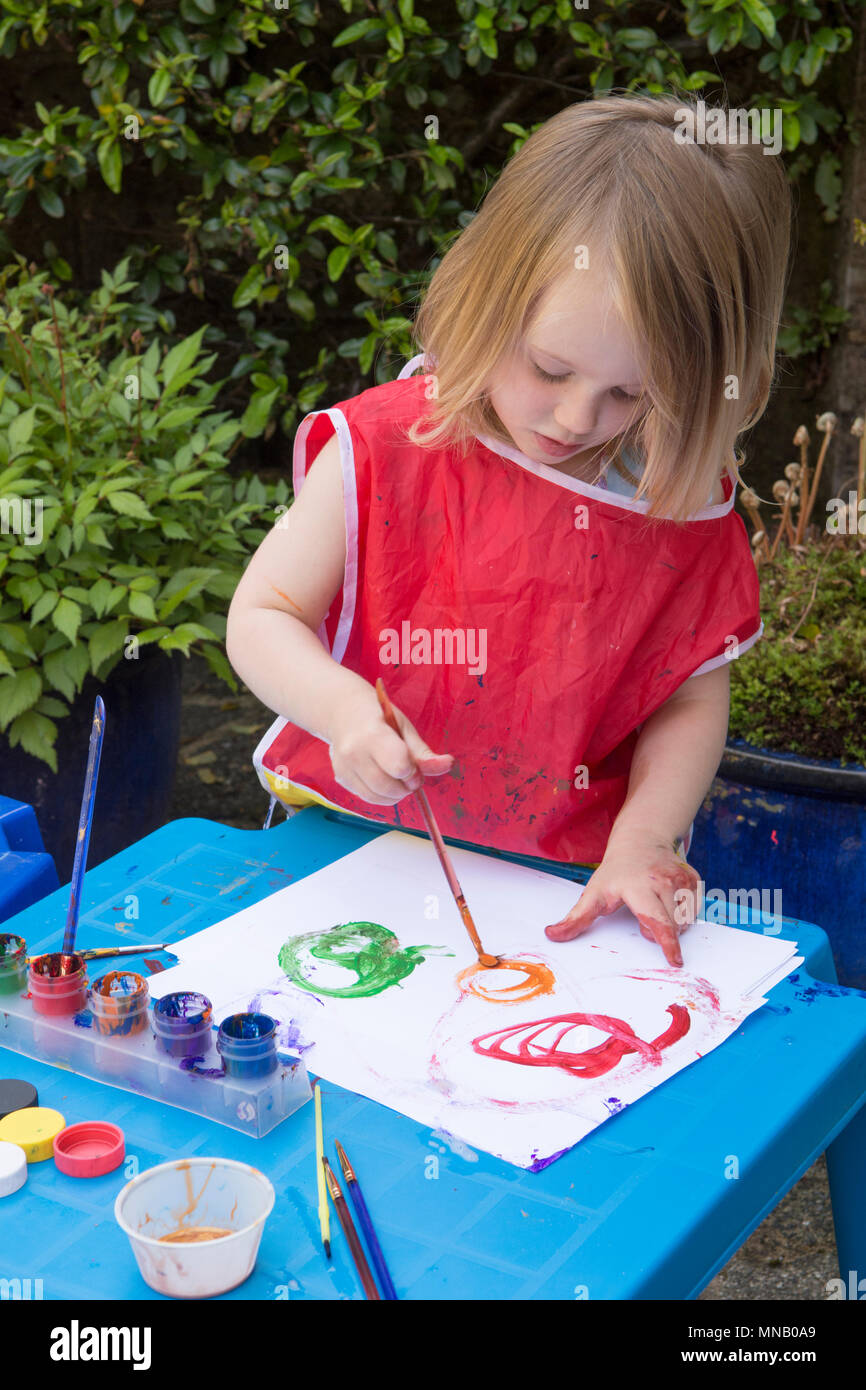 Fillette de deux ans et les modèles photos peinture à l'aquarelle peintures dans jardin, obtenir de la peinture sur les mains. Des vêtements de protection. Banque D'Images