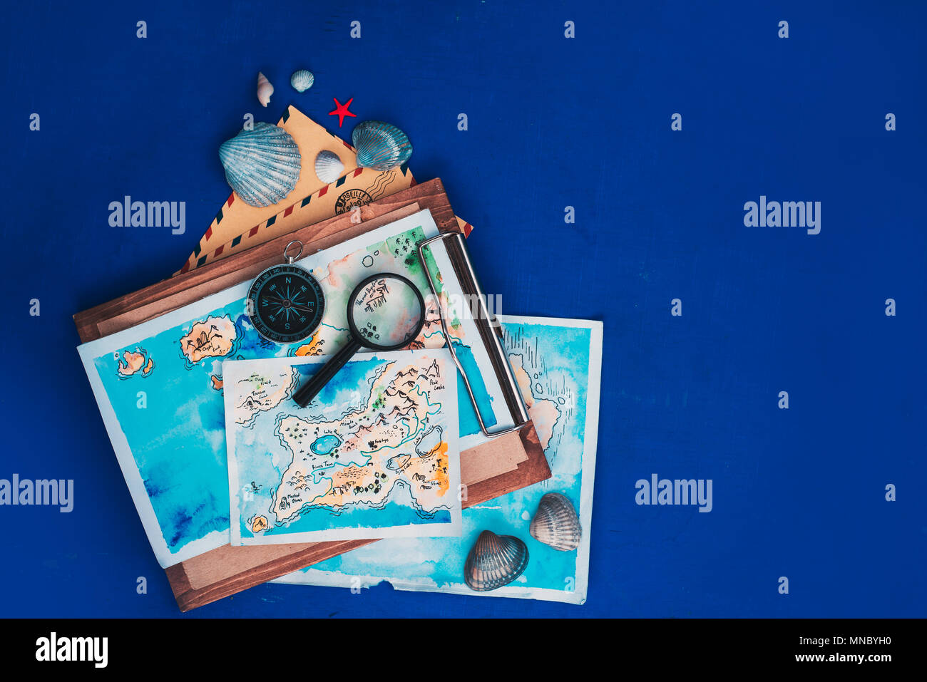 Les voyages et l'exploration de la mer concept. Cartes aquarelle sur un presse-papiers en bois, boussole et loupe télévision déposer sur un fond bleu marine avec copie s Banque D'Images