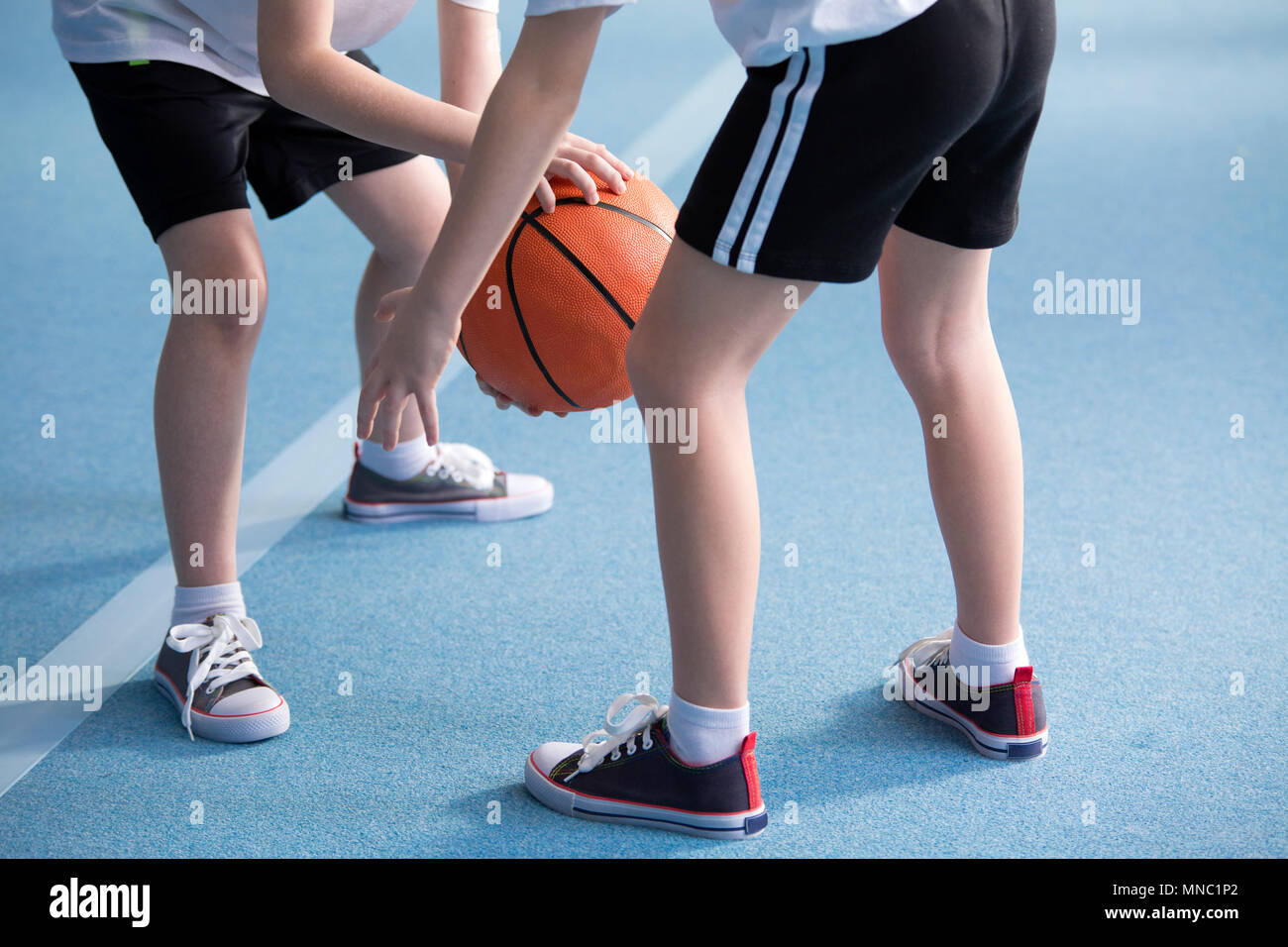 Gros plan sur les jeunes enfants portant des vêtements de l'école apprendre à dribbler un ballon de basket-ball au cours d'éducation physique à l'étage avec salle de sport blue Banque D'Images