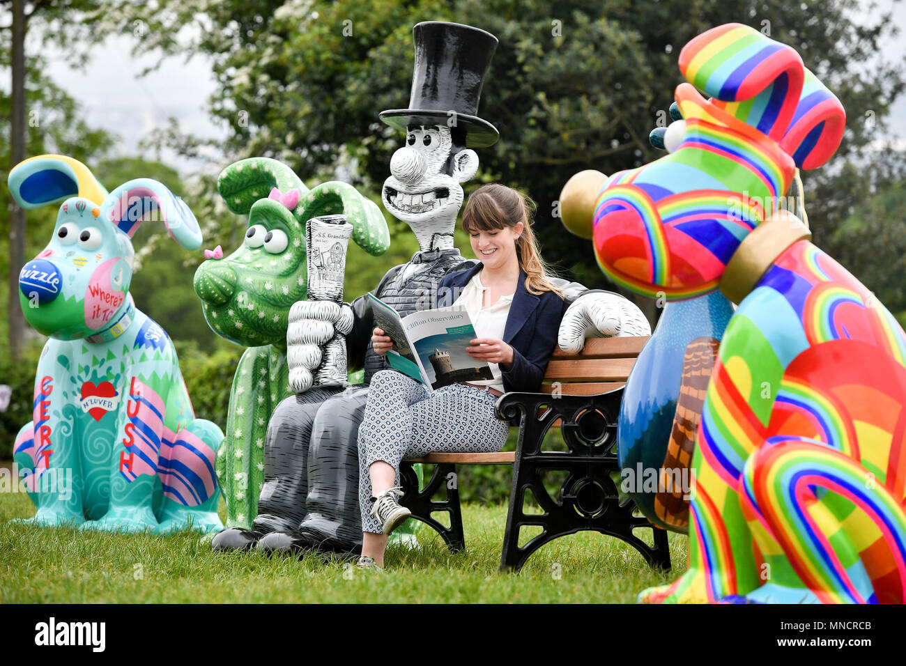 Une femme assise et lit sur un banc entouré de personnages d'Ardman animation de Wallace & Gromit comme Grand appel, l'association caritative de l'Hôpital pour enfants de Bristol, révèle les lieux où ses plus de soixante sculptures de Wallace, Gromit et Feathers McGraw seront placées dans toute la ville de Bristol. Banque D'Images