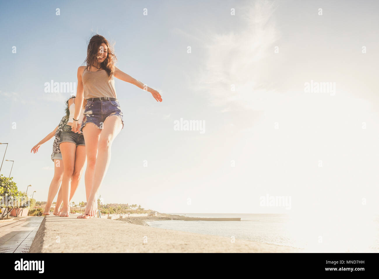 Trois jeunes femmes amis marcher ensemble sur un mur près de la plage à Ténérife. Profitez des locations sous un ciel bleu avec un soleil jaune. Mains en mains. Banque D'Images