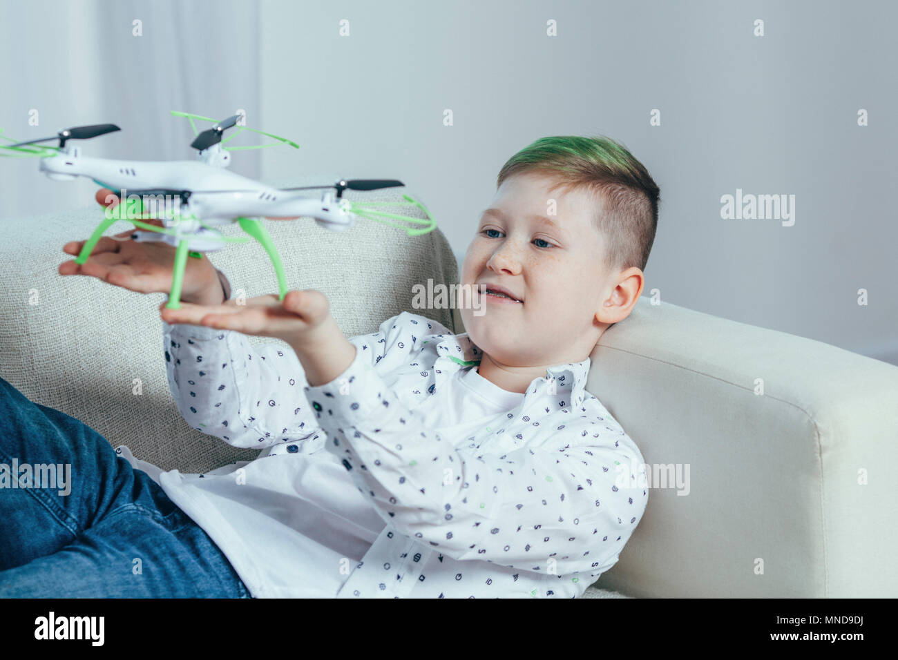 Smiling boy lying on sofa holding drone dans la salle de séjour à la maison Banque D'Images