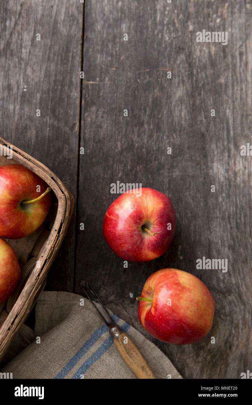 Pommes rouges sur une planche en bois avec un couteau économe et un panier Banque D'Images